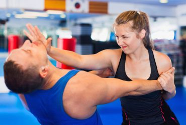 Bold positive  woman is training with man on the self-defense course in gym.